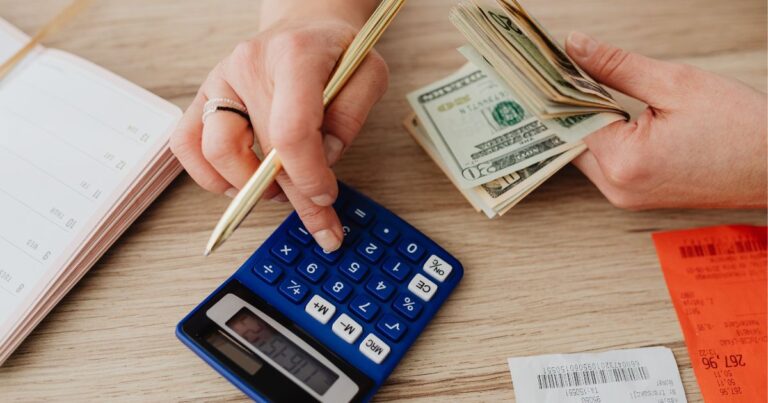 Persona calculando la diferencia entre activos y pasivos con calculadora, dinero en efectivo y recibos sobre la mesa