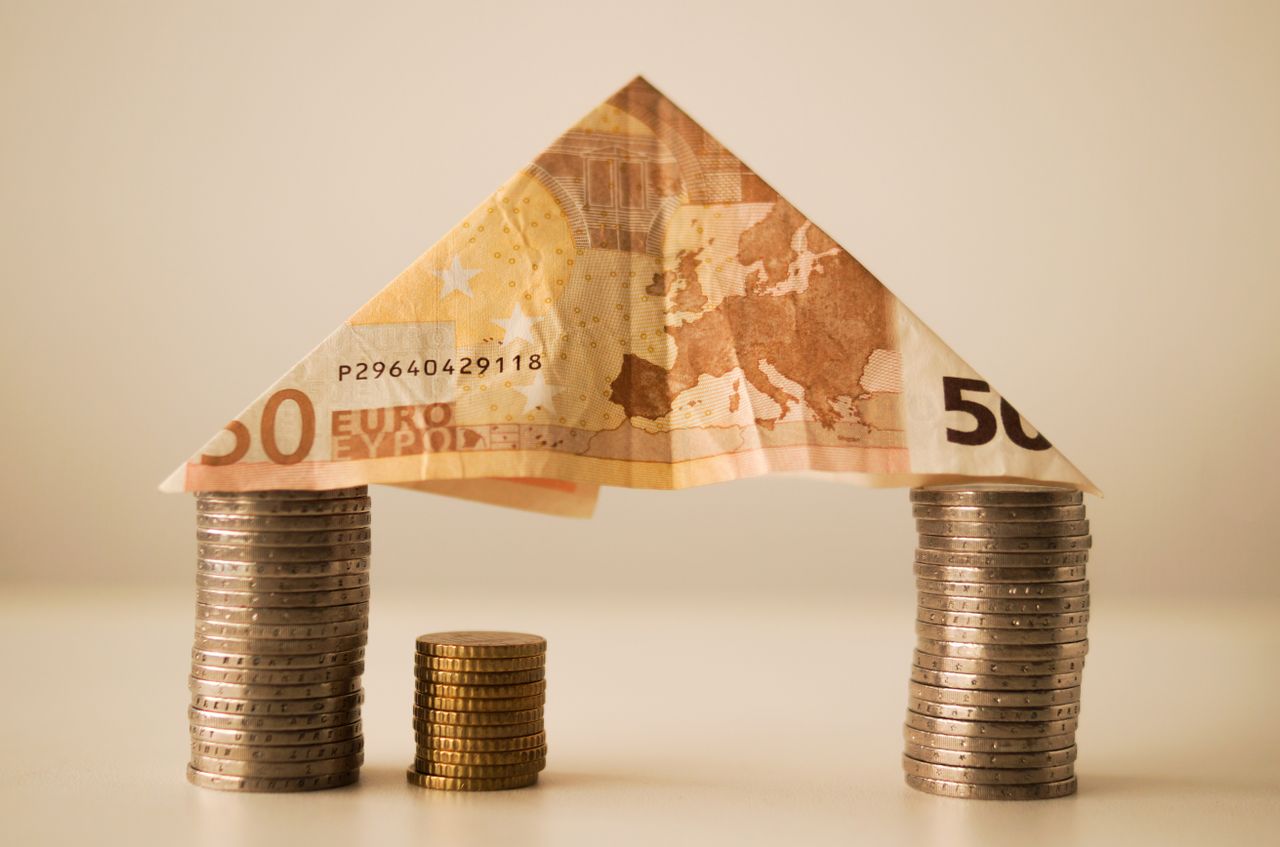 Bloques de monedas que representan la estructura de una casa y un billete doblado que representa el techo de esa casa. La imagen representa el Apalancamiento financiero en bienes raíces