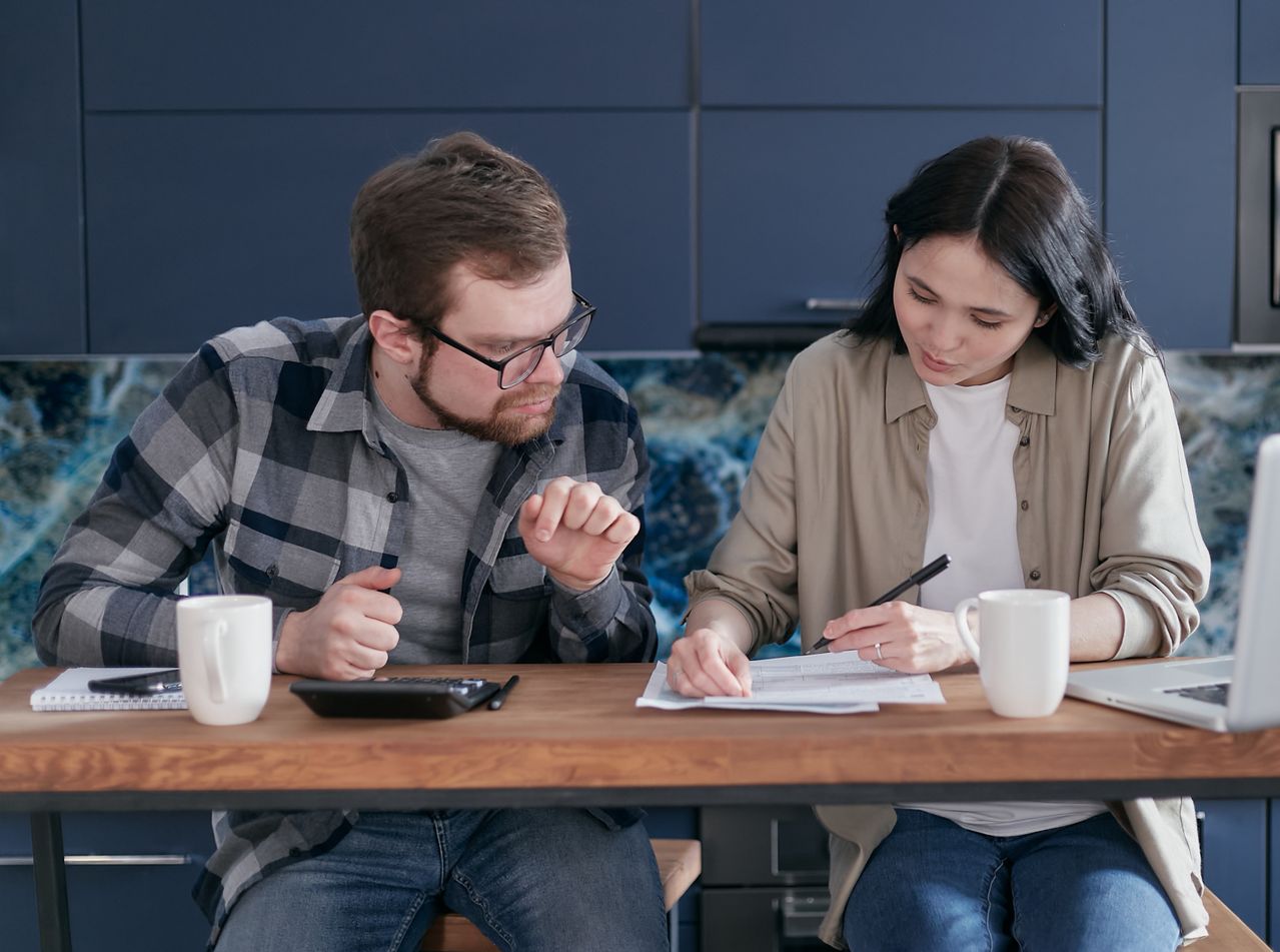 Pareja revisando juntos su presupuesto personal y los gastos del hogar en la mesa de la cocina