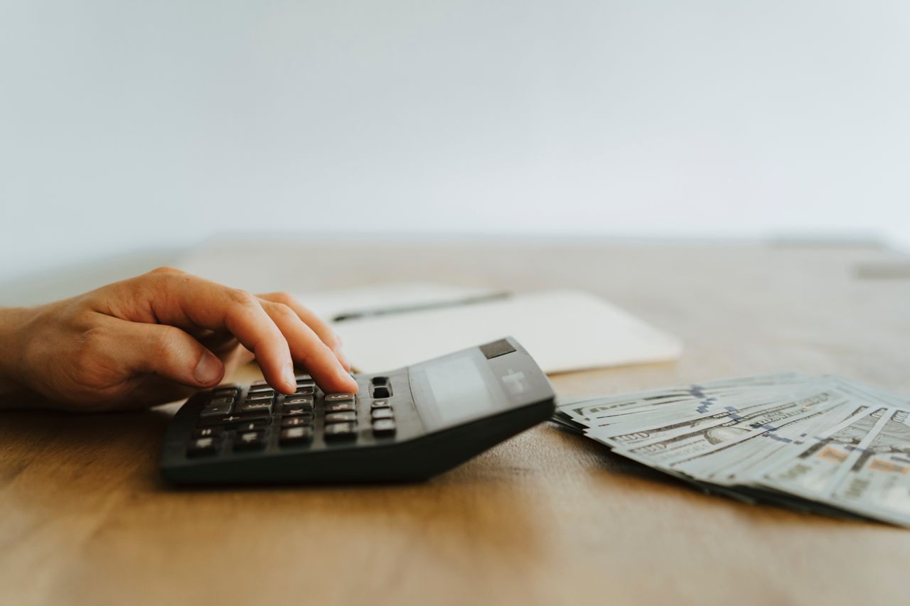Mano calculando finanzas con calculadora y billetes sobre la mesa, ilustrando el cálculo de ahorro versus inversión a 10 años