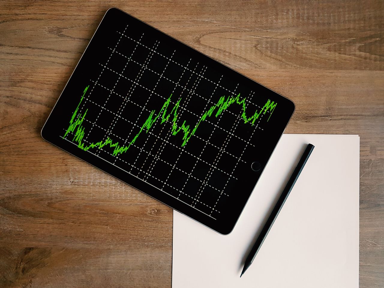 Gráfico de crecimiento en tablet junto a papel y lápiz, ilustrando cómo proyectar el interés compuesto
