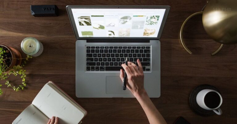 Persona con un computador creado su sitio web para marketing de afiliados. En la mesa tiene una libreta con apuntes