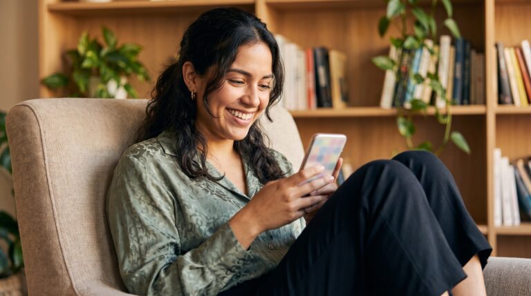 Mujer sonriendo mientras usa la app de eToro desde su teléfono, cómodamente en un sillón